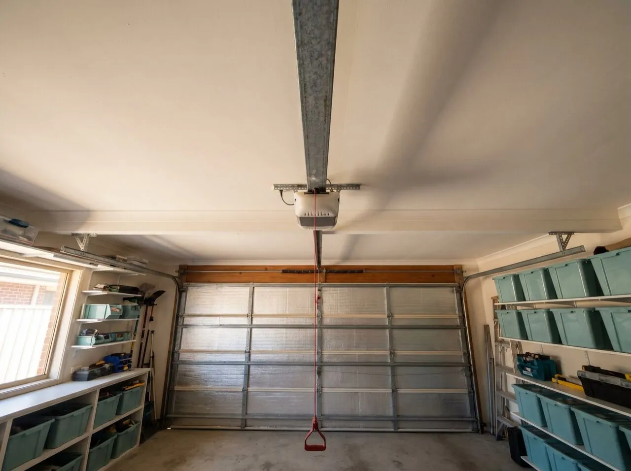A ceiling-mounted garage door opener and drive rail with the red manual release cord